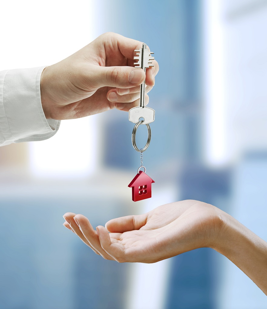 Man is handing a house key to a woman. Key with a keychain in the shape of the house